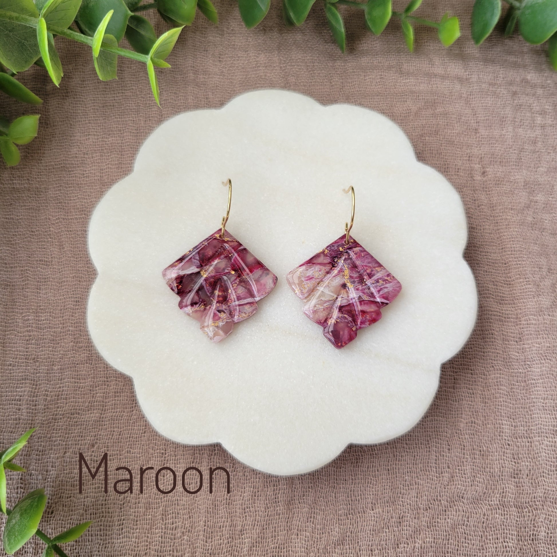 Top view of a pair of maroon marbled earrings displayed on a white round scalloped tray.