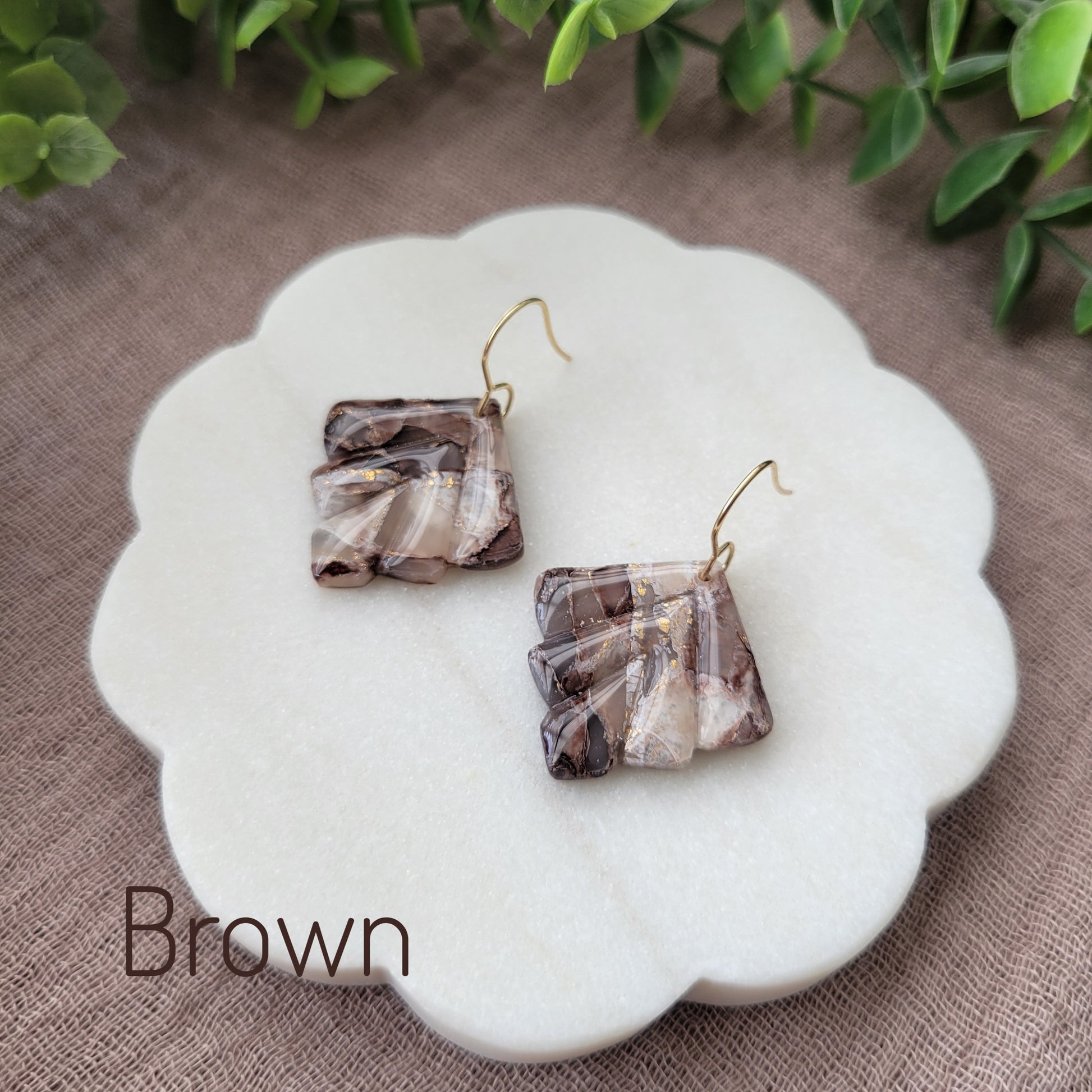 Side view of a pair of brown marbled earrings displayed on a white round scalloped tray.