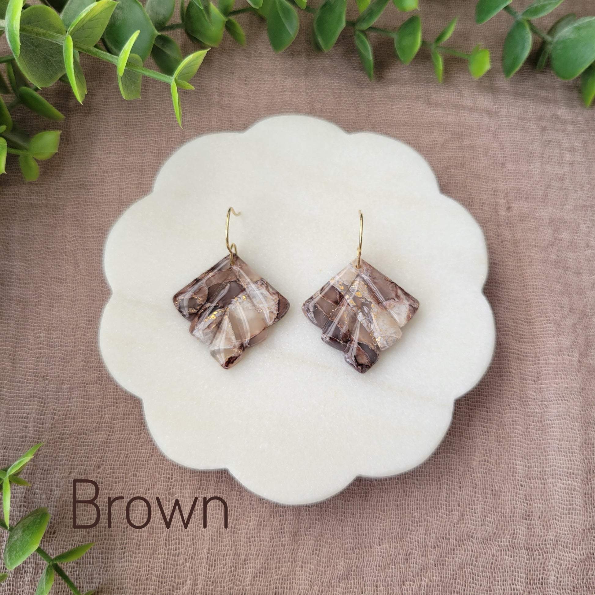 Top view of a pair of brown marbled earrings displayed on a white round scalloped tray.
