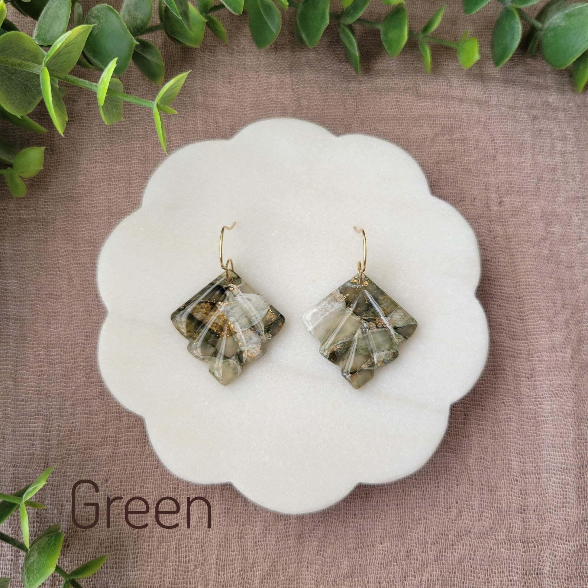Top view of a pair of green marbled earrings displayed on a white round scalloped tray.