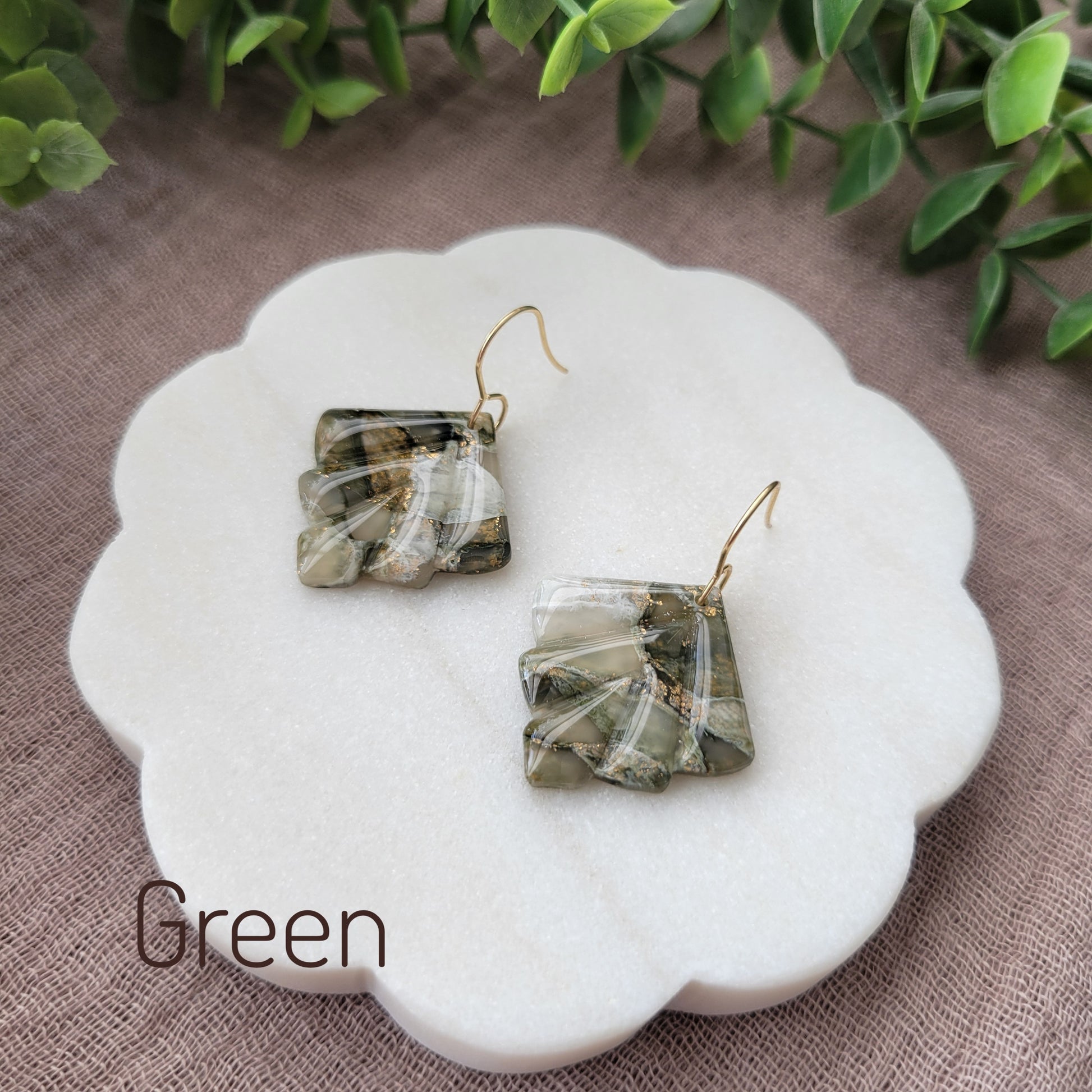 Side view of a pair of green marbled earrings displayed on a white round scalloped tray.