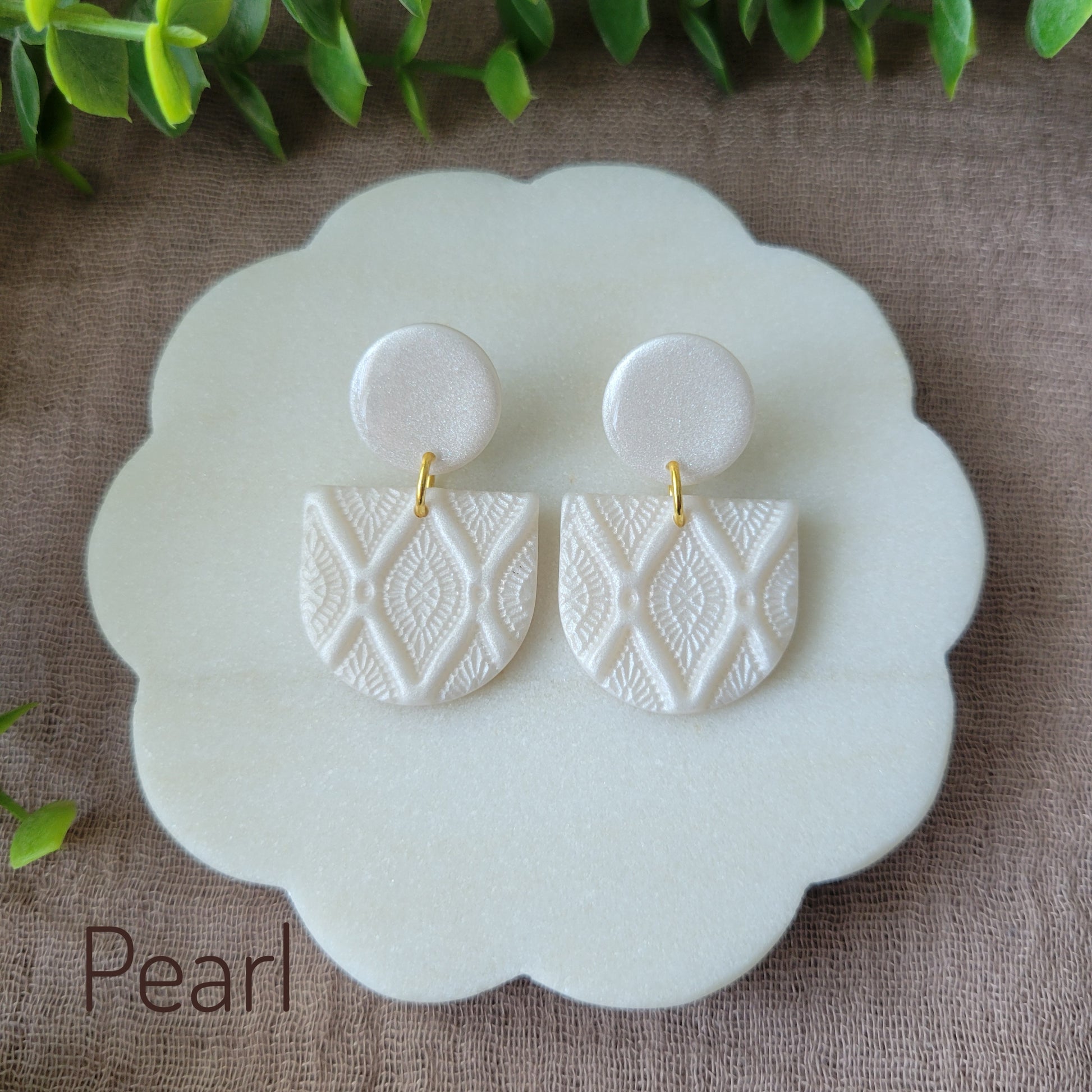 Top view of a pair of pearl earrings with deco diamond texture displayed on a white round scalloped tray.