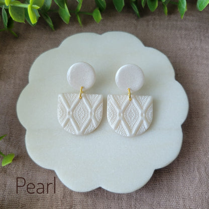Top view of a pair of pearl earrings with deco diamond texture displayed on a white round scalloped tray.