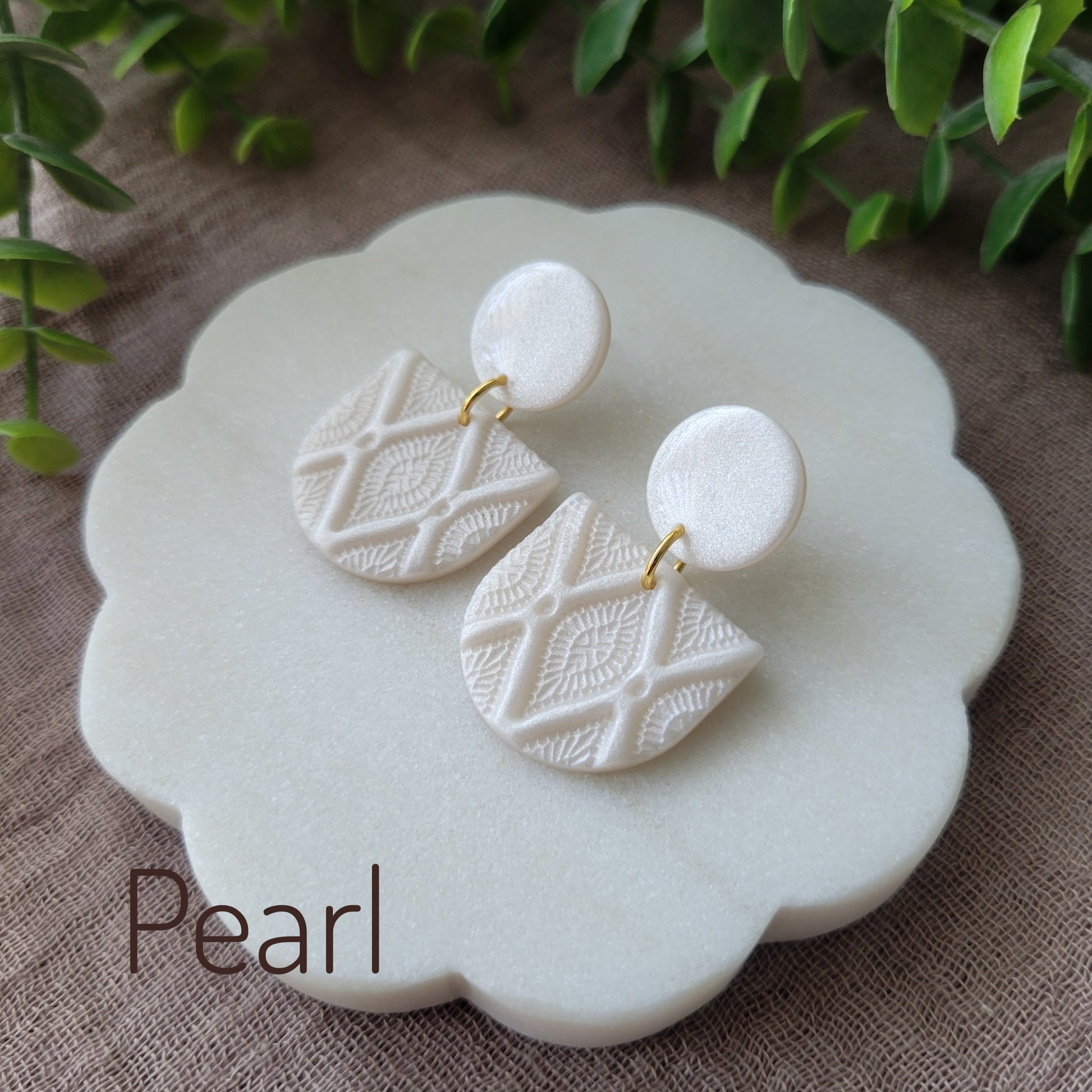 Side view of a pair of pearl earrings with deco diamond texture displayed on a white round scalloped tray.