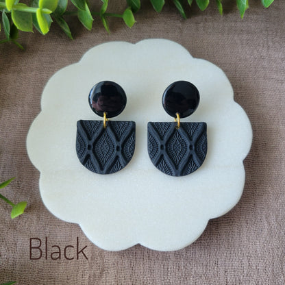 Top view of a pair of black earrings with deco diamond texture displayed on a white round scalloped tray.