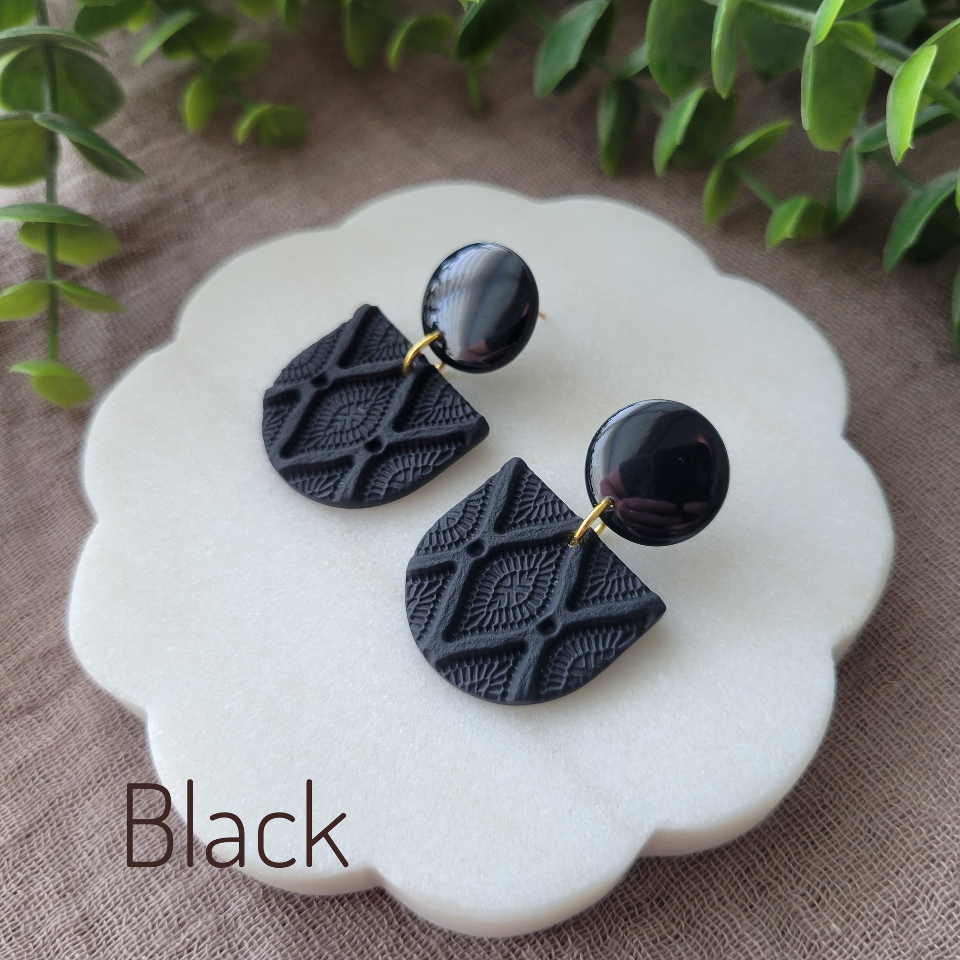Side view of a pair of black earrings with deco diamond texture displayed on a white round scalloped tray.