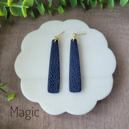 Top view of a pair of dark blue pillar earrings with interwoven leaves texture displayed on a white round scalloped tray.