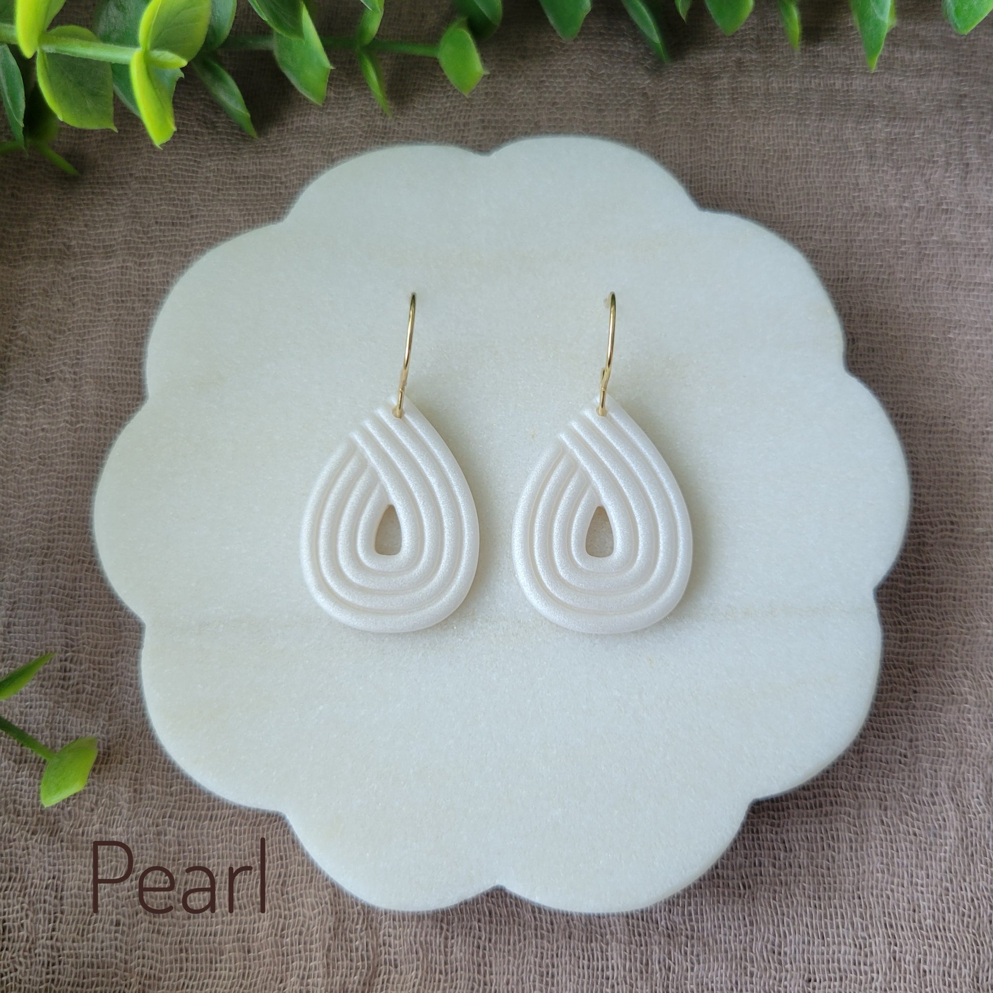Top view of a pair of pearl embossed teardrop earrings displayed on a round white scalloped tray.