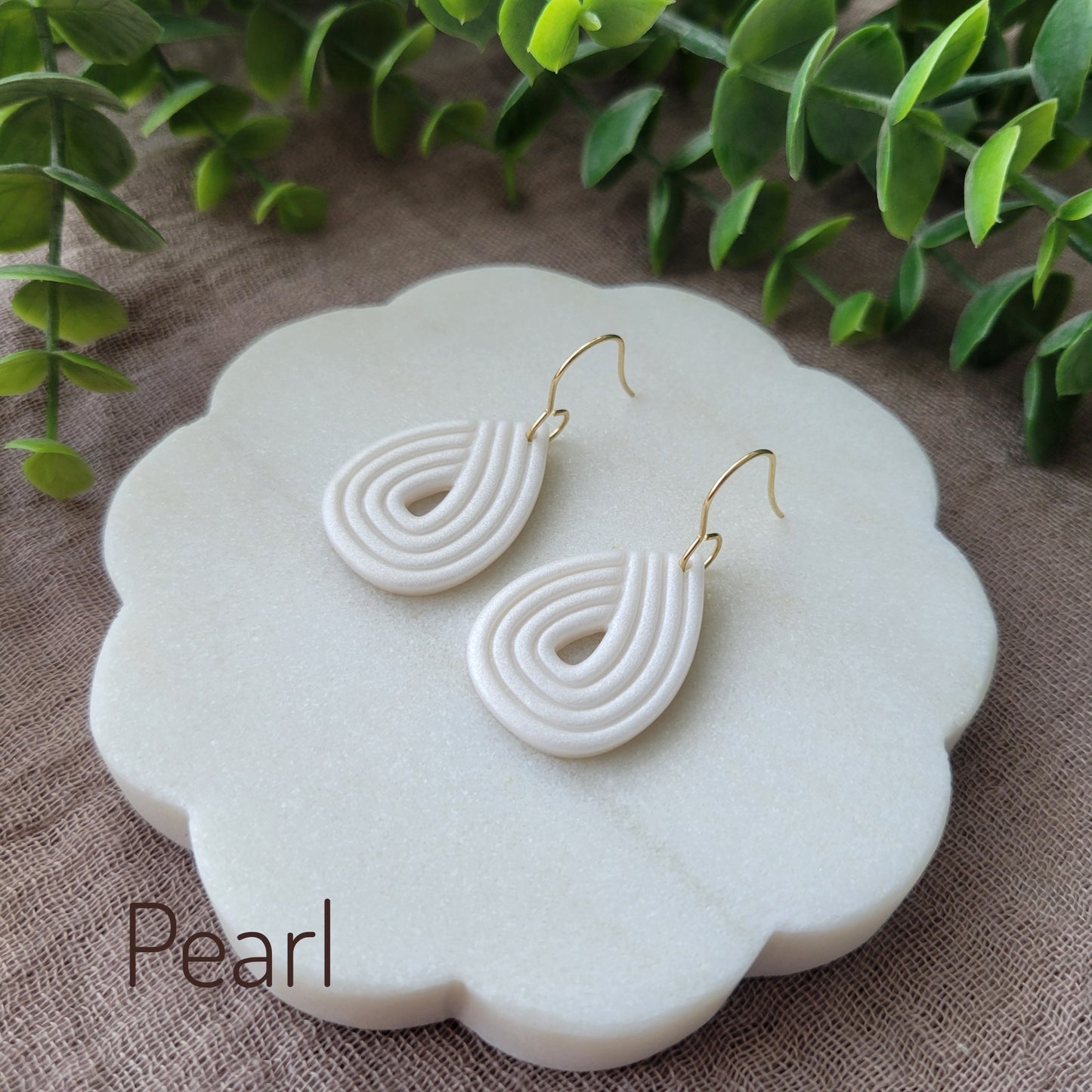 Side view of a pair of pearl embossed teardrop earrings displayed on a round white scalloped tray.