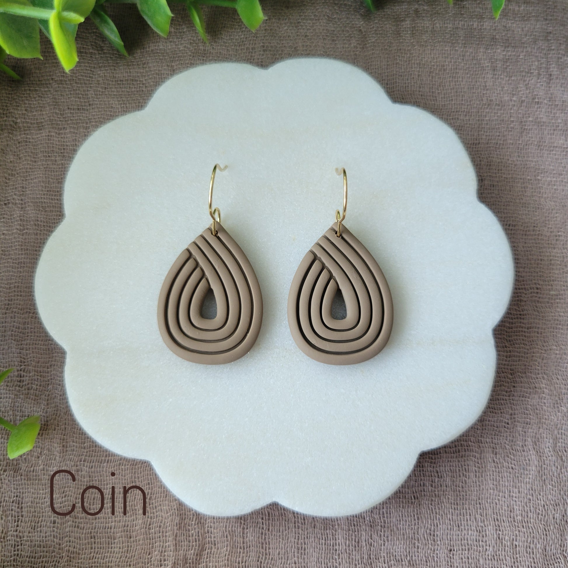 Top view of a pair of brown embossed teardrop earrings displayed on a round scalloped white tray.
