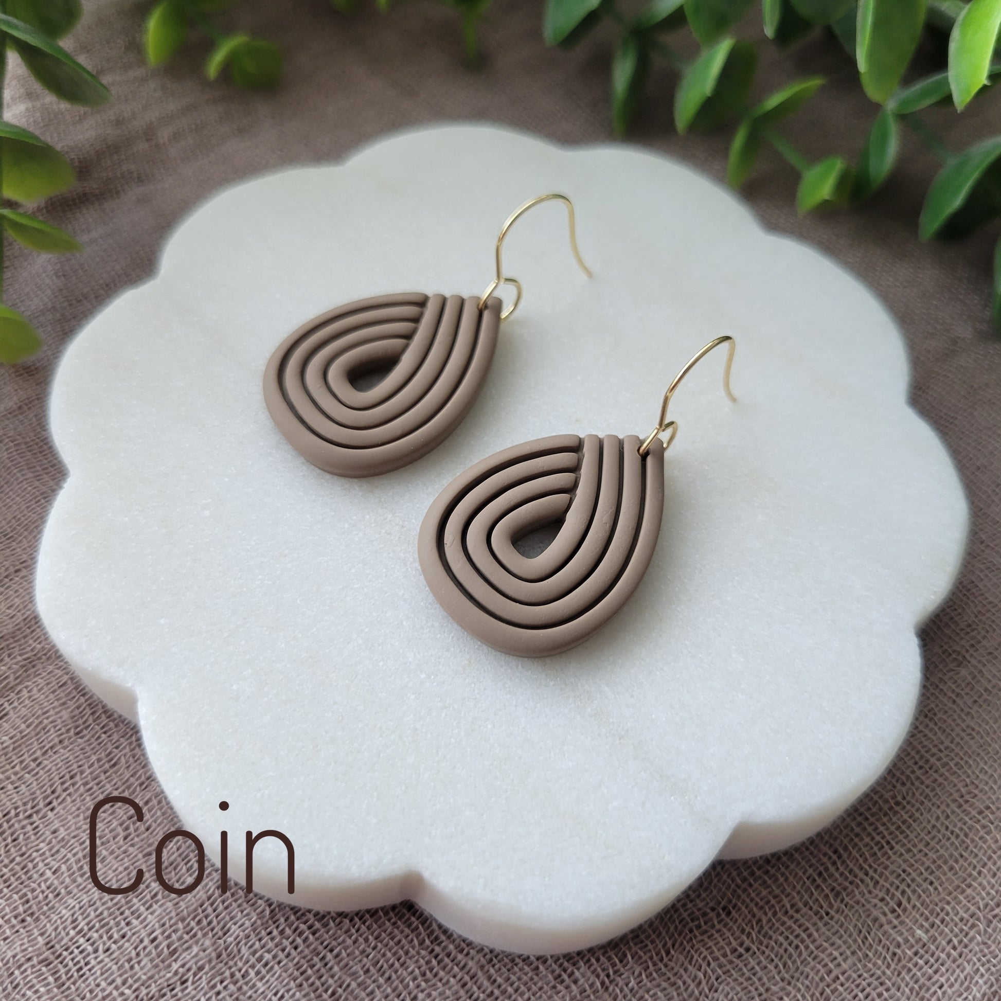 Side view of a pair of brown embossed teardrop earrings displayed on a round scalloped white tray.