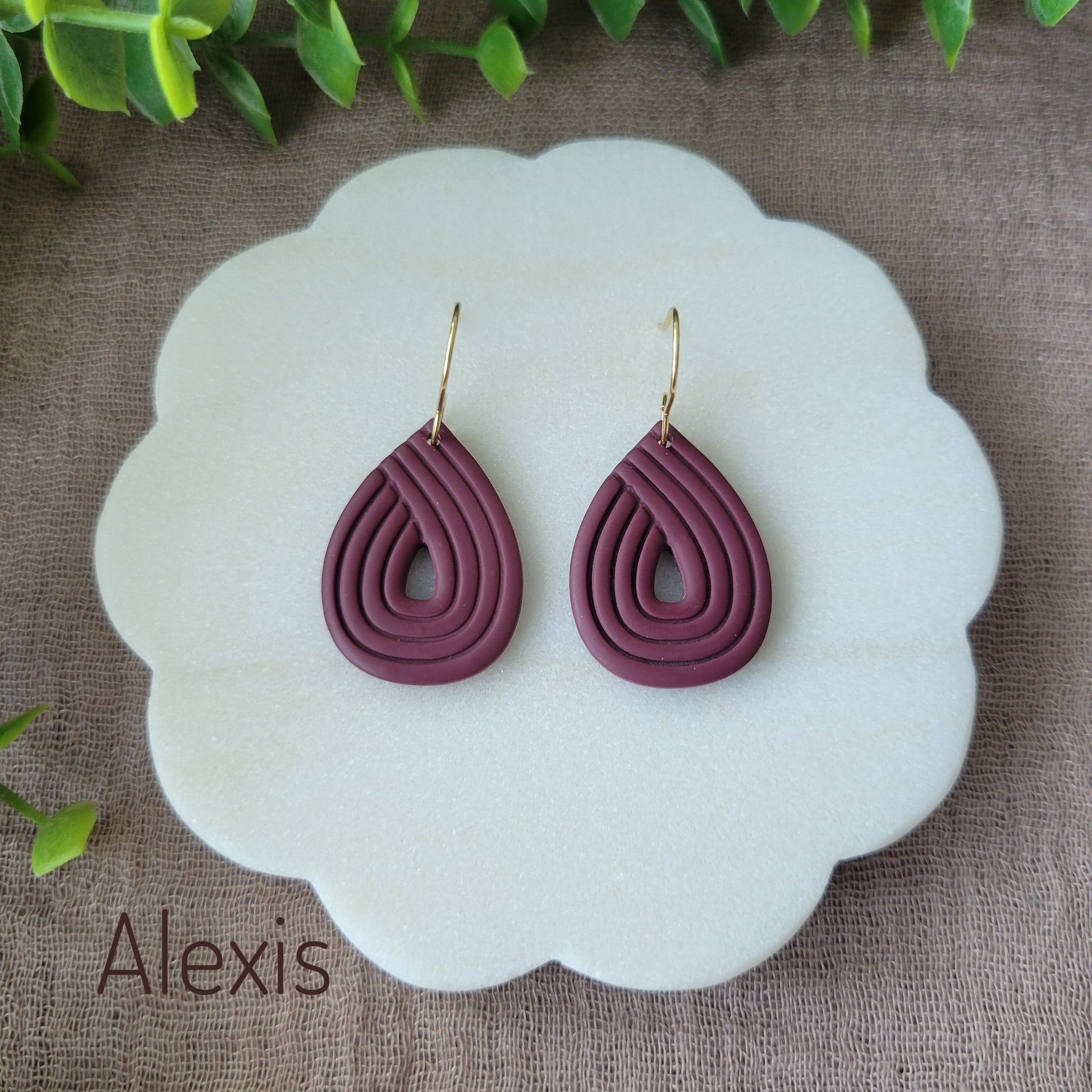 Top view of a pair of reddish purple embossed teardrop earrings displayed on a round scalloped white tray.
