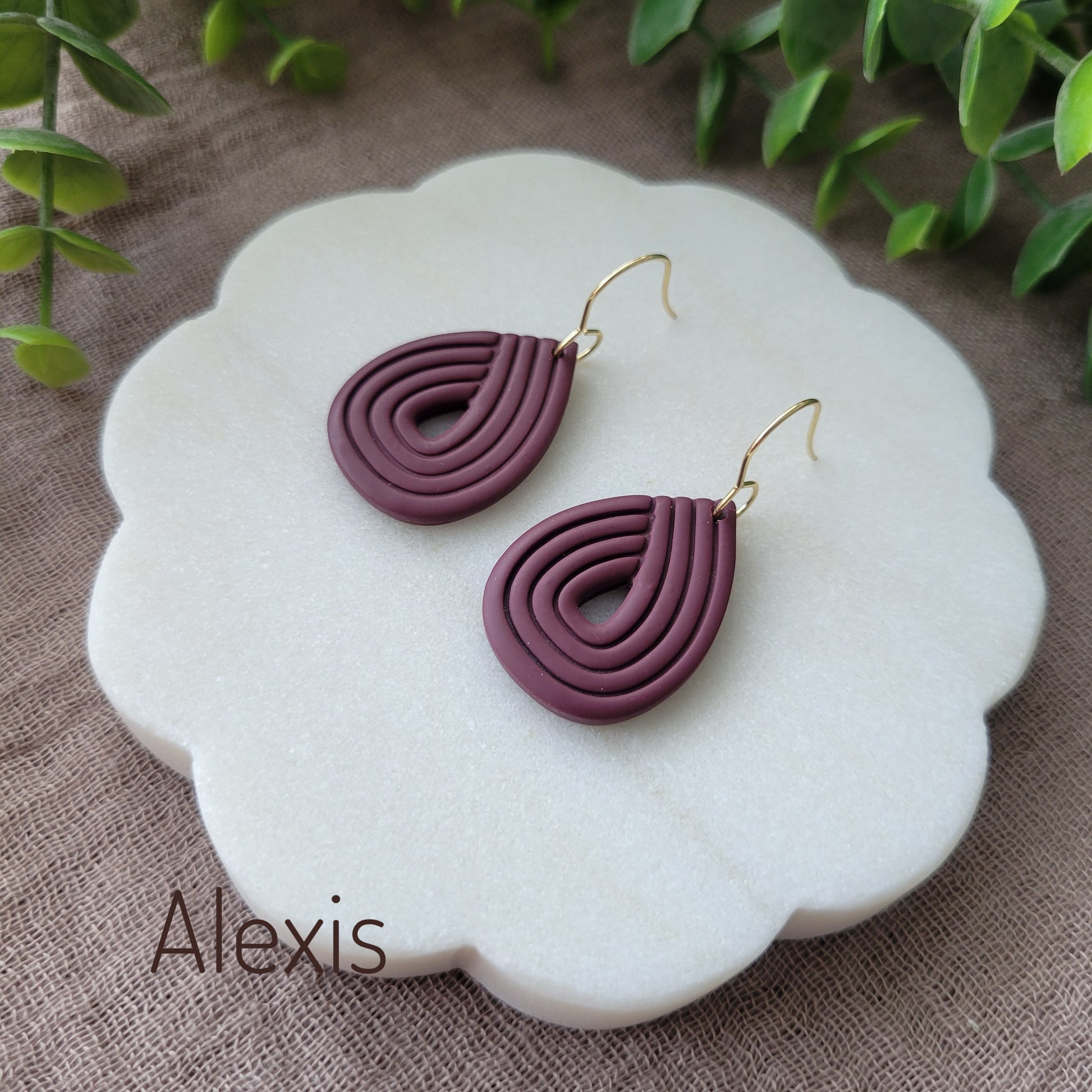 Side view of a pair of reddish purple embossed earrings displayed on a round scalloped white tray.