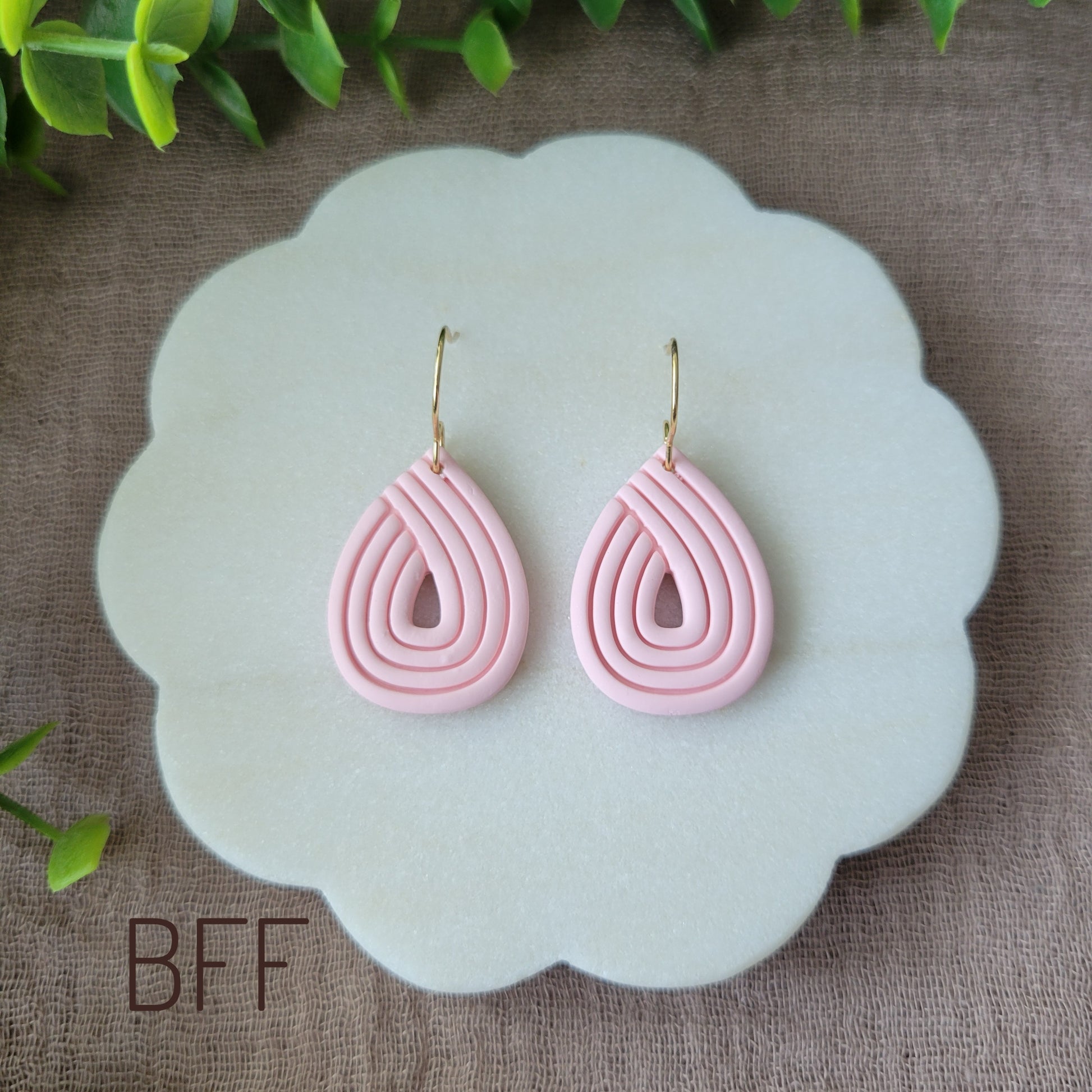 Top view of a pair of pink embossed teardrop earrings displayed on a round white scalloped tray.