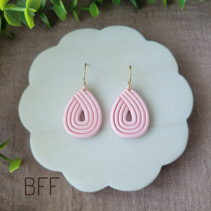 Top view of a pair of pink embossed teardrop earrings displayed on a round white scalloped tray.