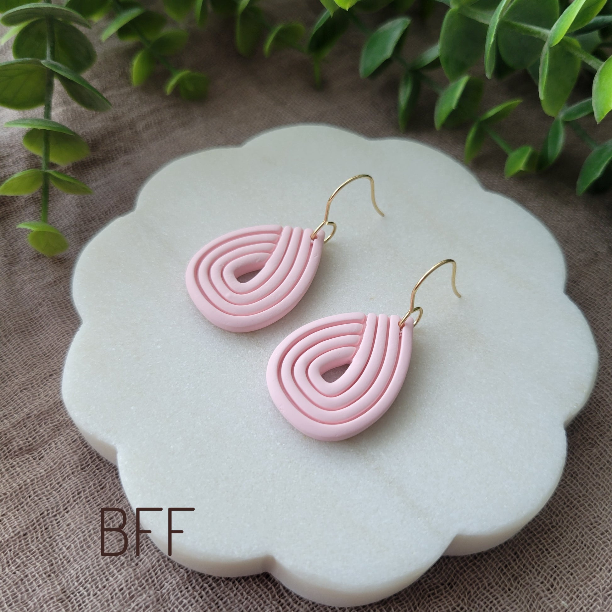 Side view of a pink pair of embossed teardrop earrings displayed on a round white scalloped tray.
