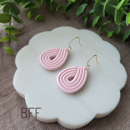 Side view of a pink pair of embossed teardrop earrings displayed on a round white scalloped tray.