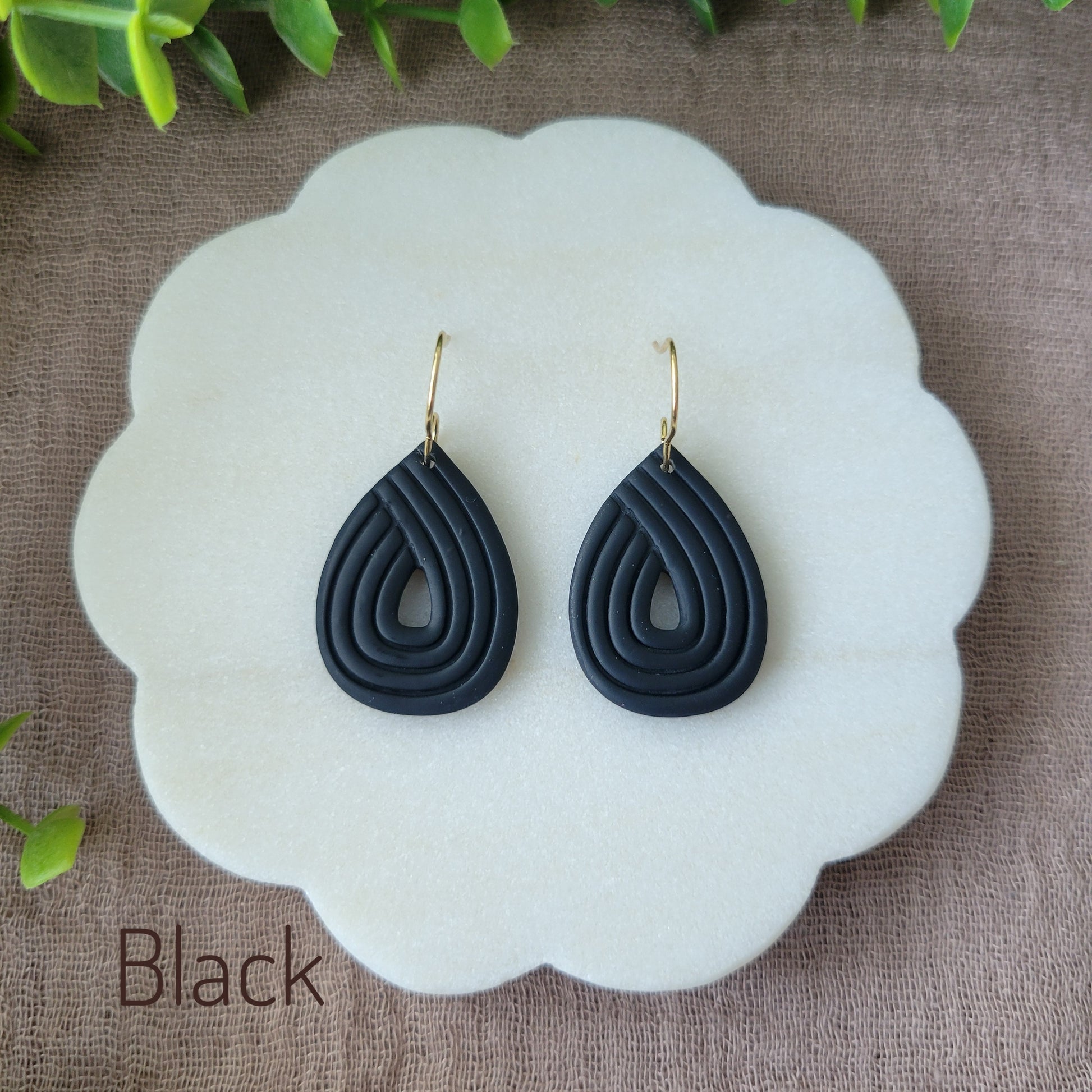 Top view of a pair of black embossed teardrop earrings displayed on a round scalloped white tray.