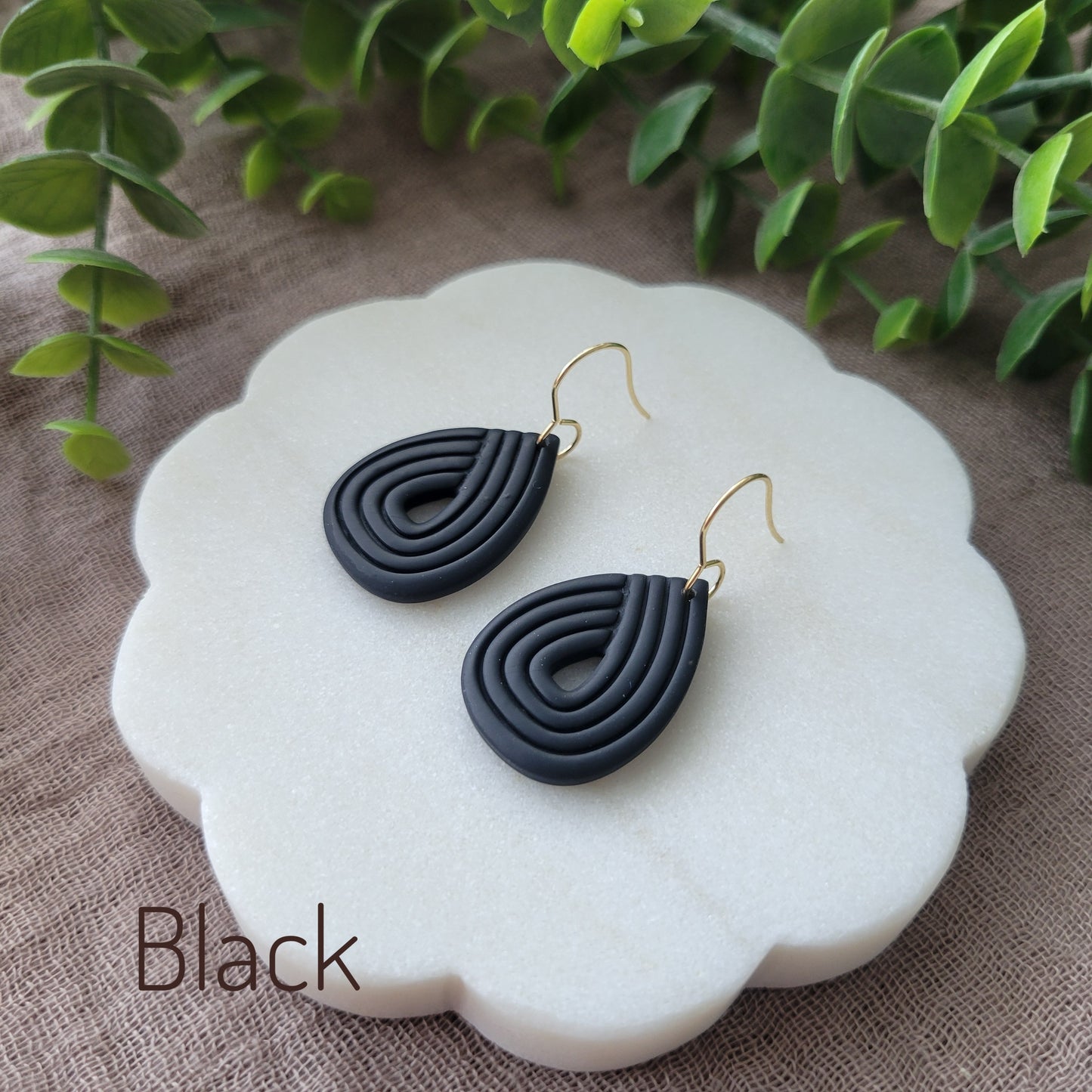 Side view of a pair of black embossed teardrop earrings displayed on a round scalloped white tray.