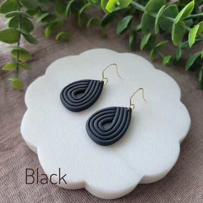 Side view of a pair of black embossed teardrop earrings displayed on a round scalloped white tray.