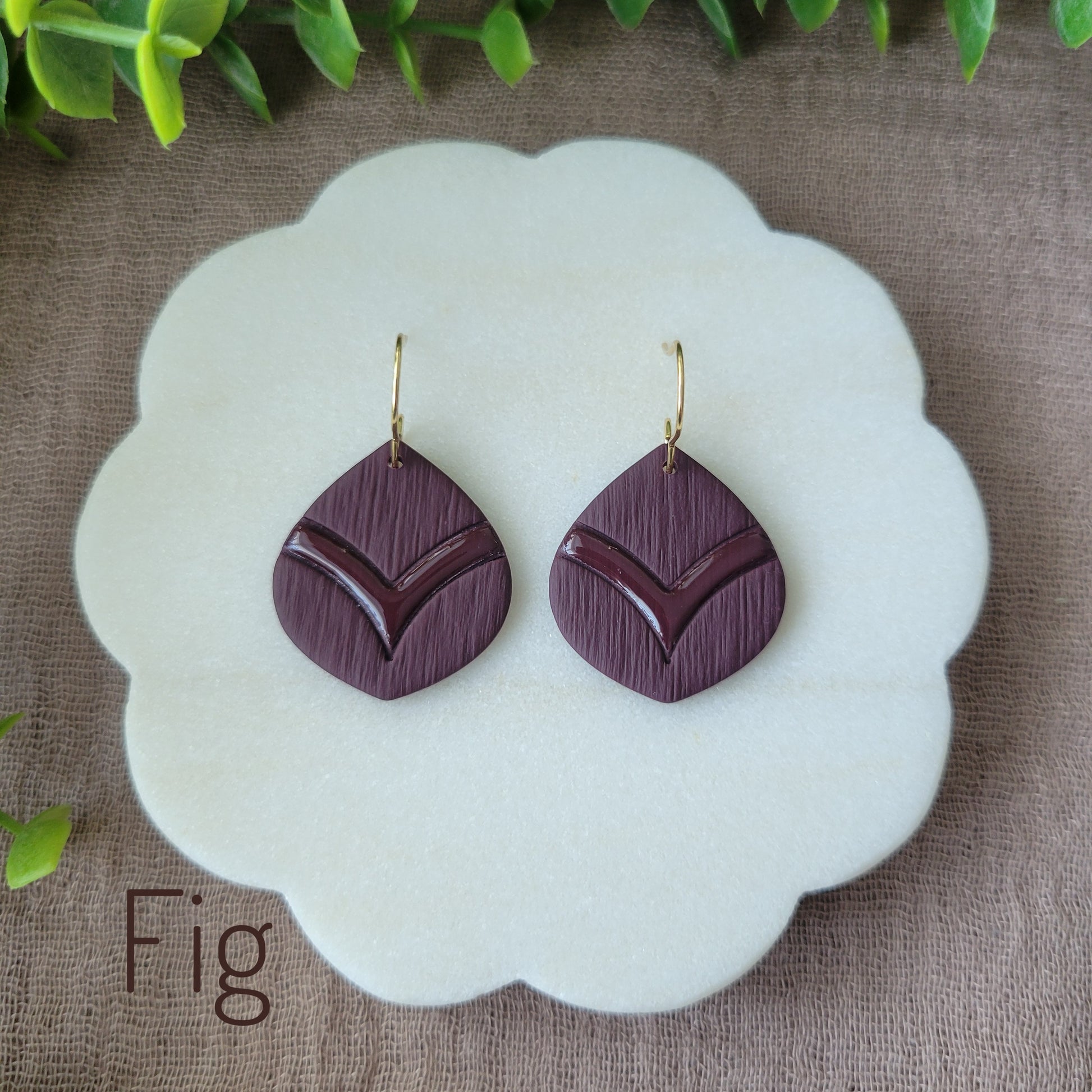 Top view of a pair of dark reddish purple embossed round teardrop earrings displayed on a white round scalloped tray.