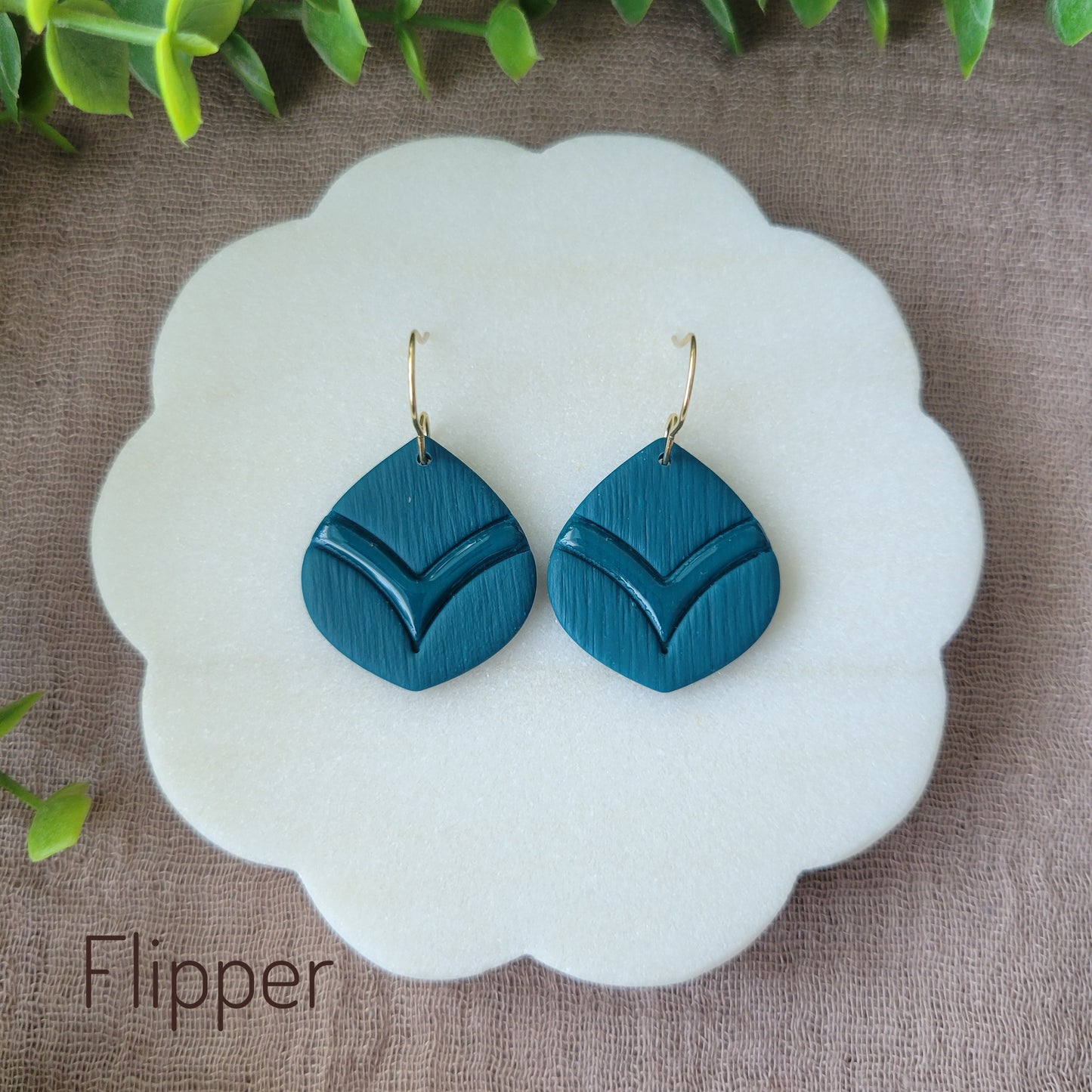 Top view of a pair of blue embossed round teardrop earrings displayed on a white round scalloped tray.