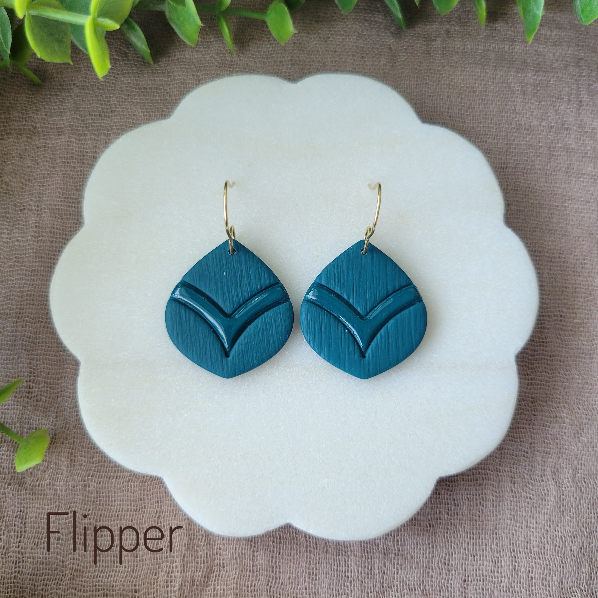 Top view of a pair of blue embossed round teardrop earrings displayed on a white round scalloped tray.