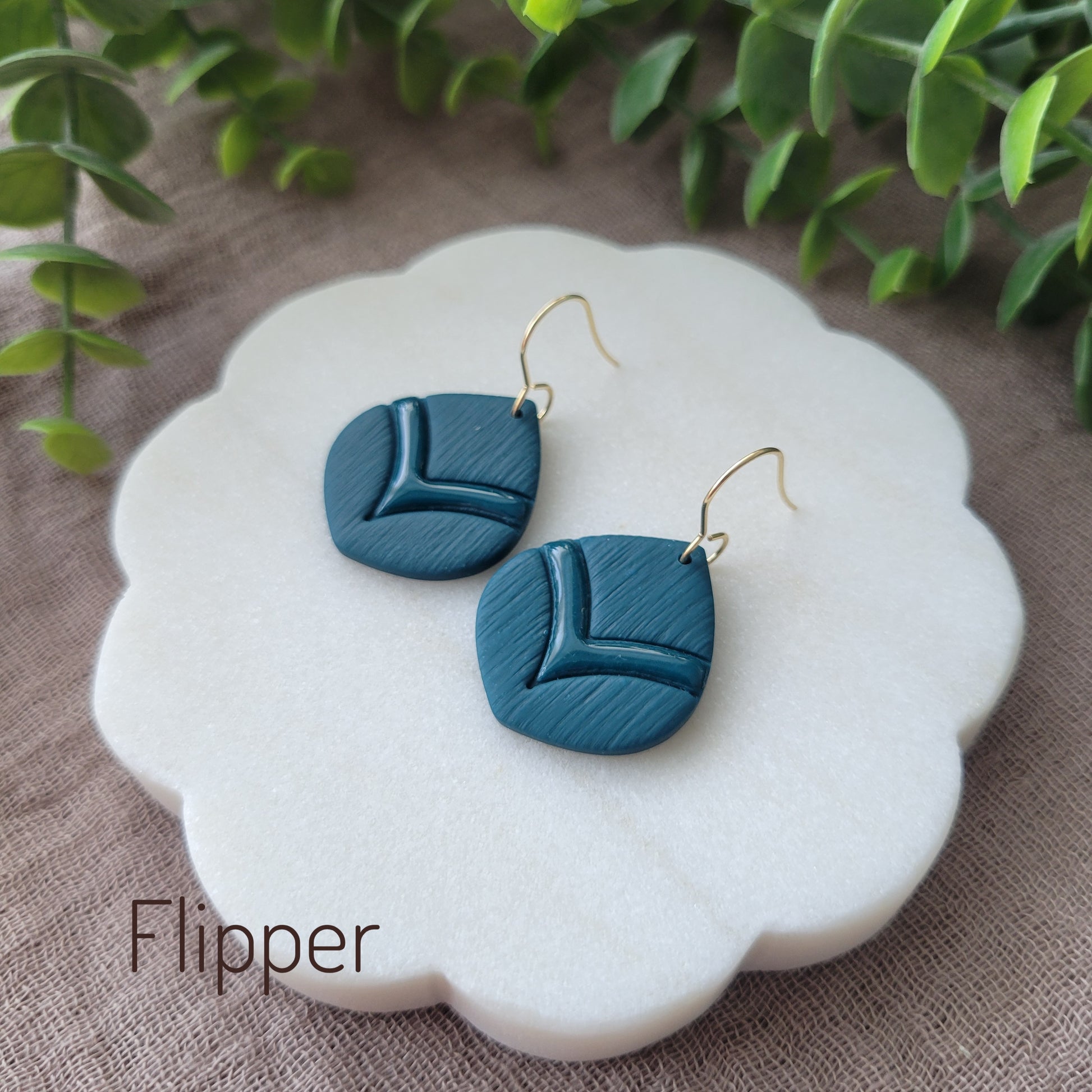 Side view of a pair of blue embossed round teardrop earrings displayed on a white round scalloped tray.