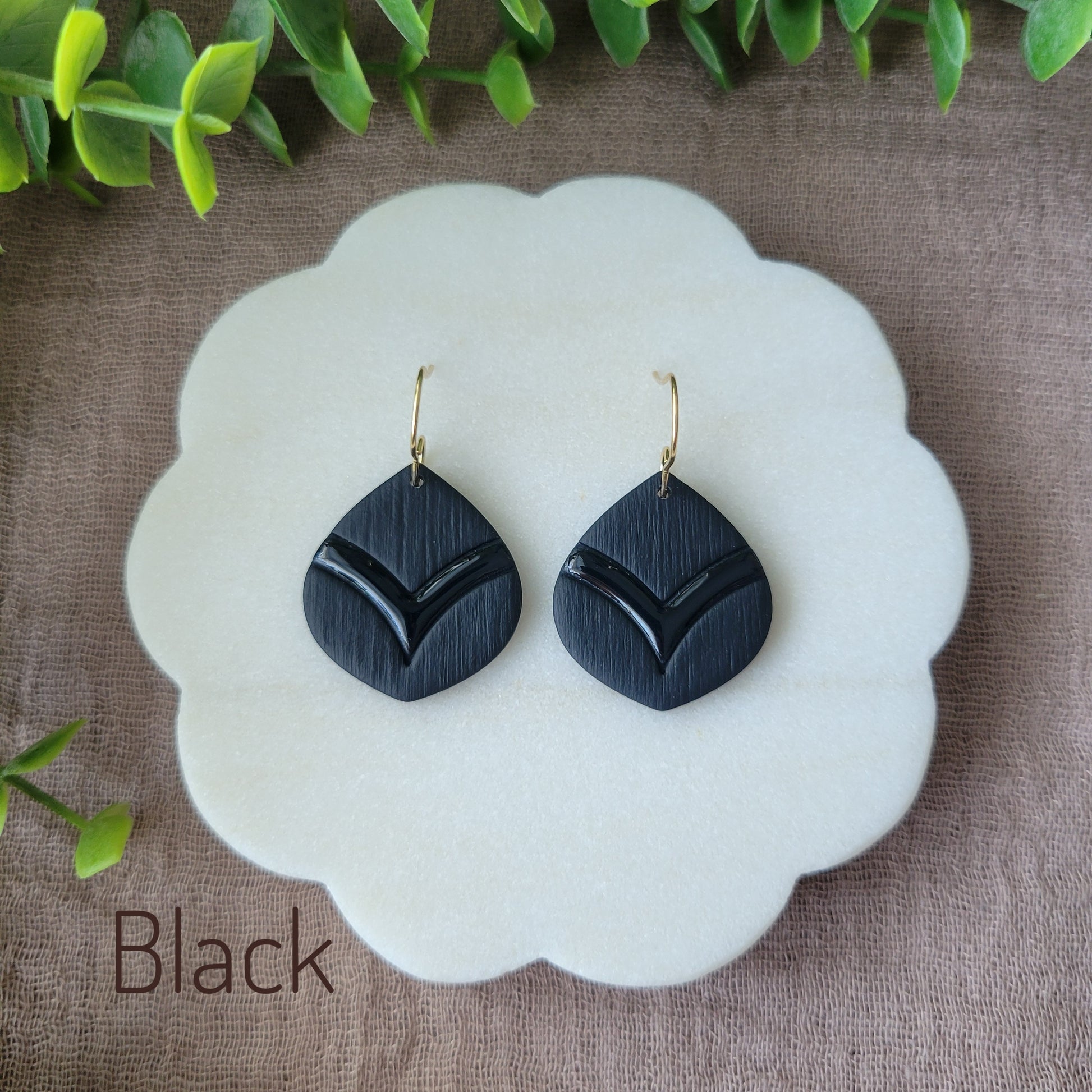 Top view of a pair of black embossed round teardrop earrings displayed on a white round scalloped tray.