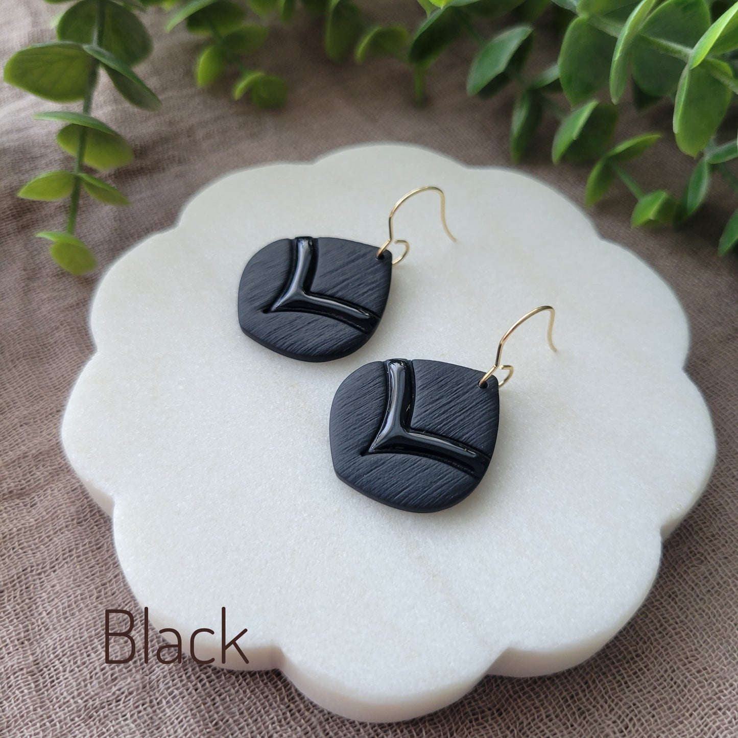 Side view of a pair of black embossed round teardrop earrings displayed on a white round scalloped tray.