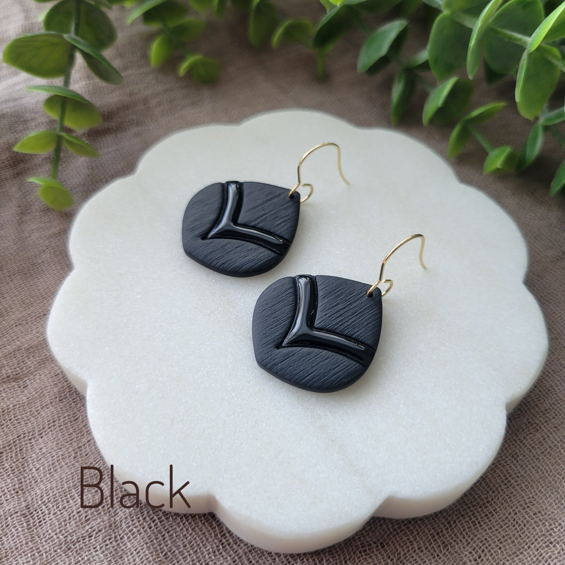 Side view of a pair of black embossed round teardrop earrings displayed on a white round scalloped tray.