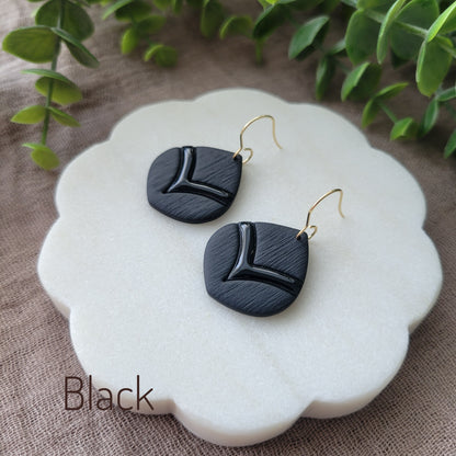 Side view of a pair of black embossed round teardrop earrings displayed on a white round scalloped tray.