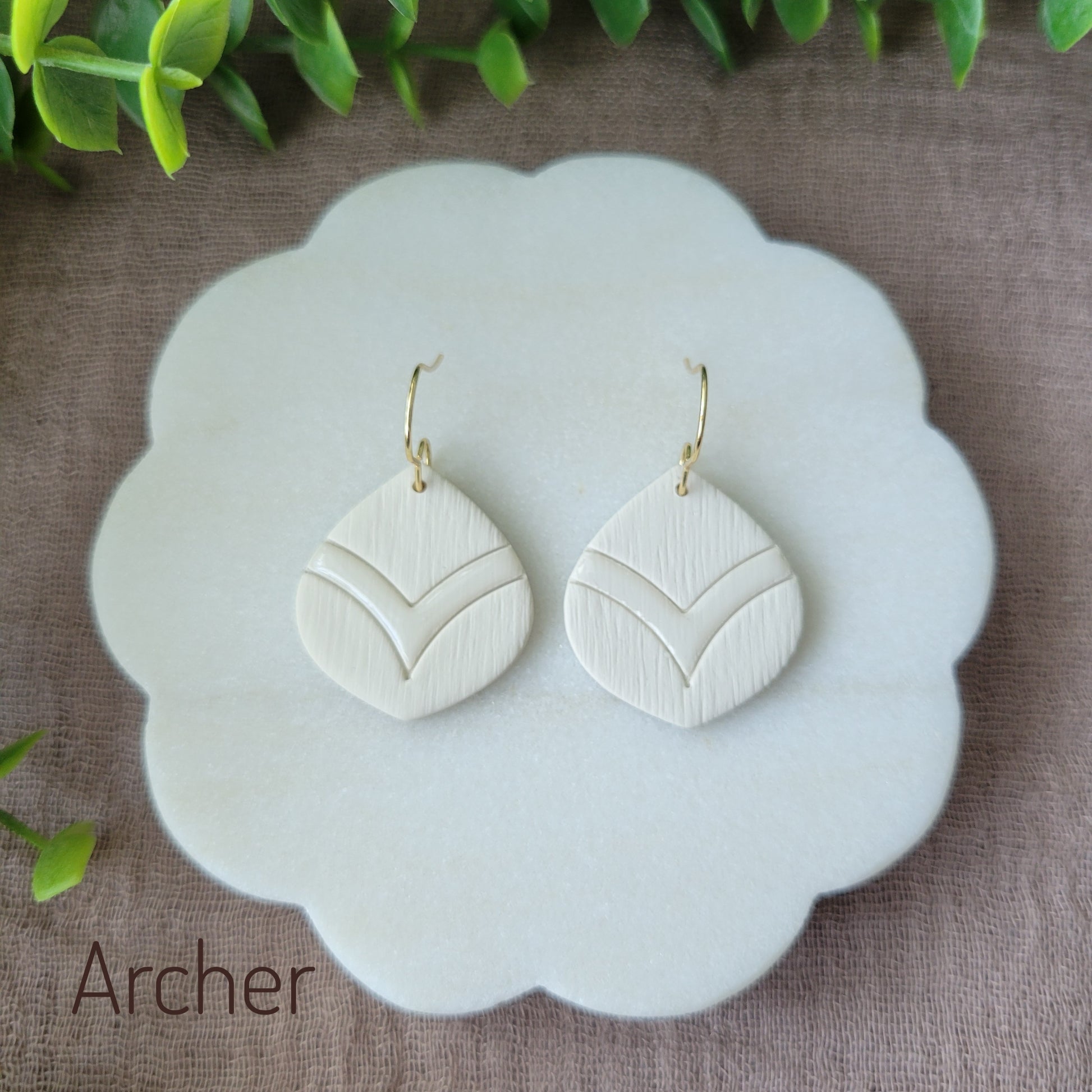 Top view of a pair of cream round embossed teardrop earrings displayed on a white round scalloped tray.
