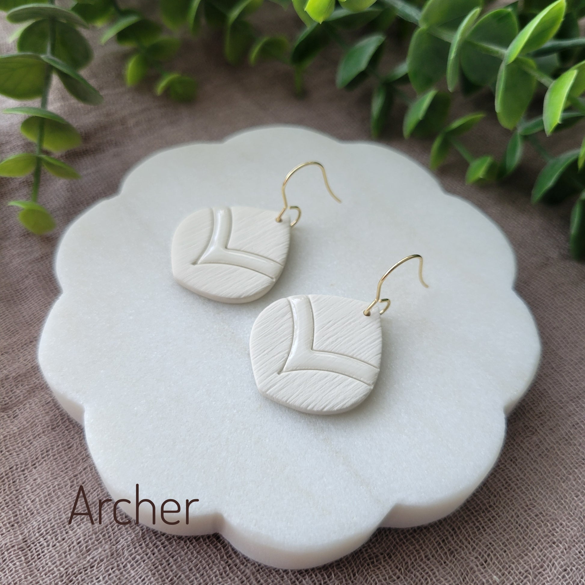 Side view of a pair of cream round embossed teardrop earrings displayed on a white round scalloped tray.