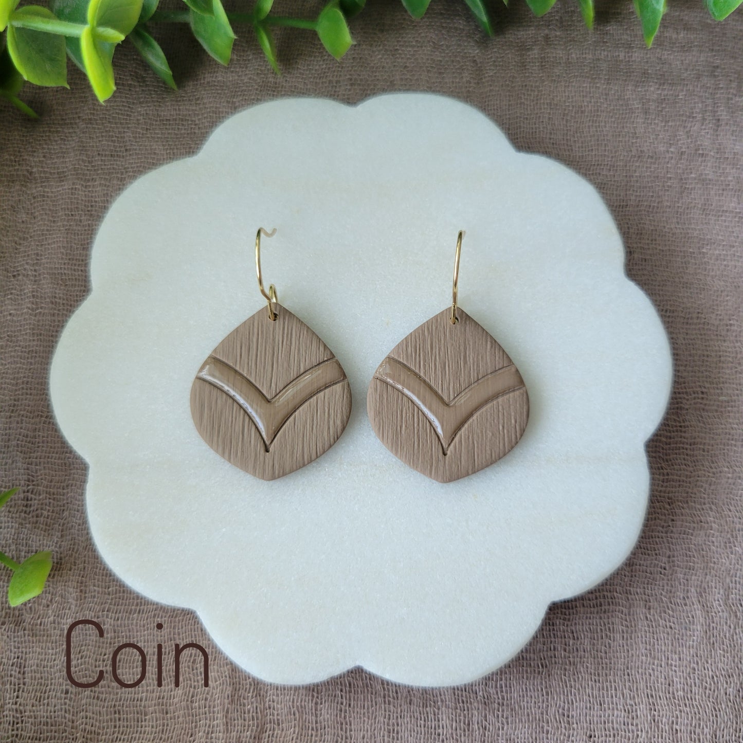 Top view of a pair of brown embossed round teardrop earrings displayed on a white round scalloped tray.