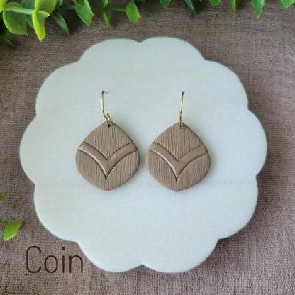 Top view of a pair of brown embossed round teardrop earrings displayed on a white round scalloped tray.