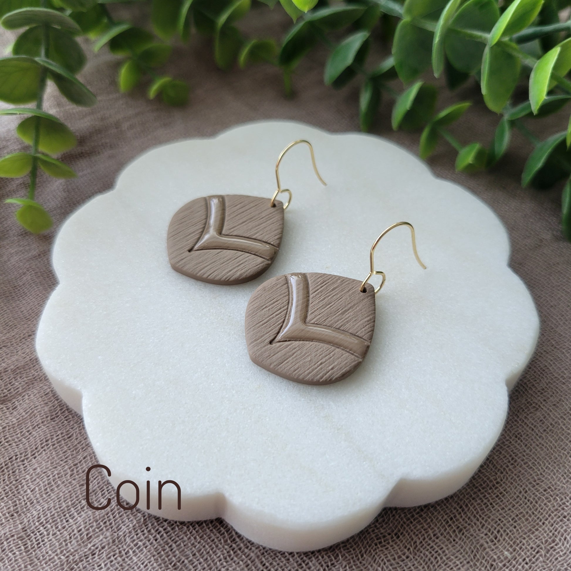 Side view of a pair of brown embossed round teardrop earrings displayed on a white round scalloped tray.