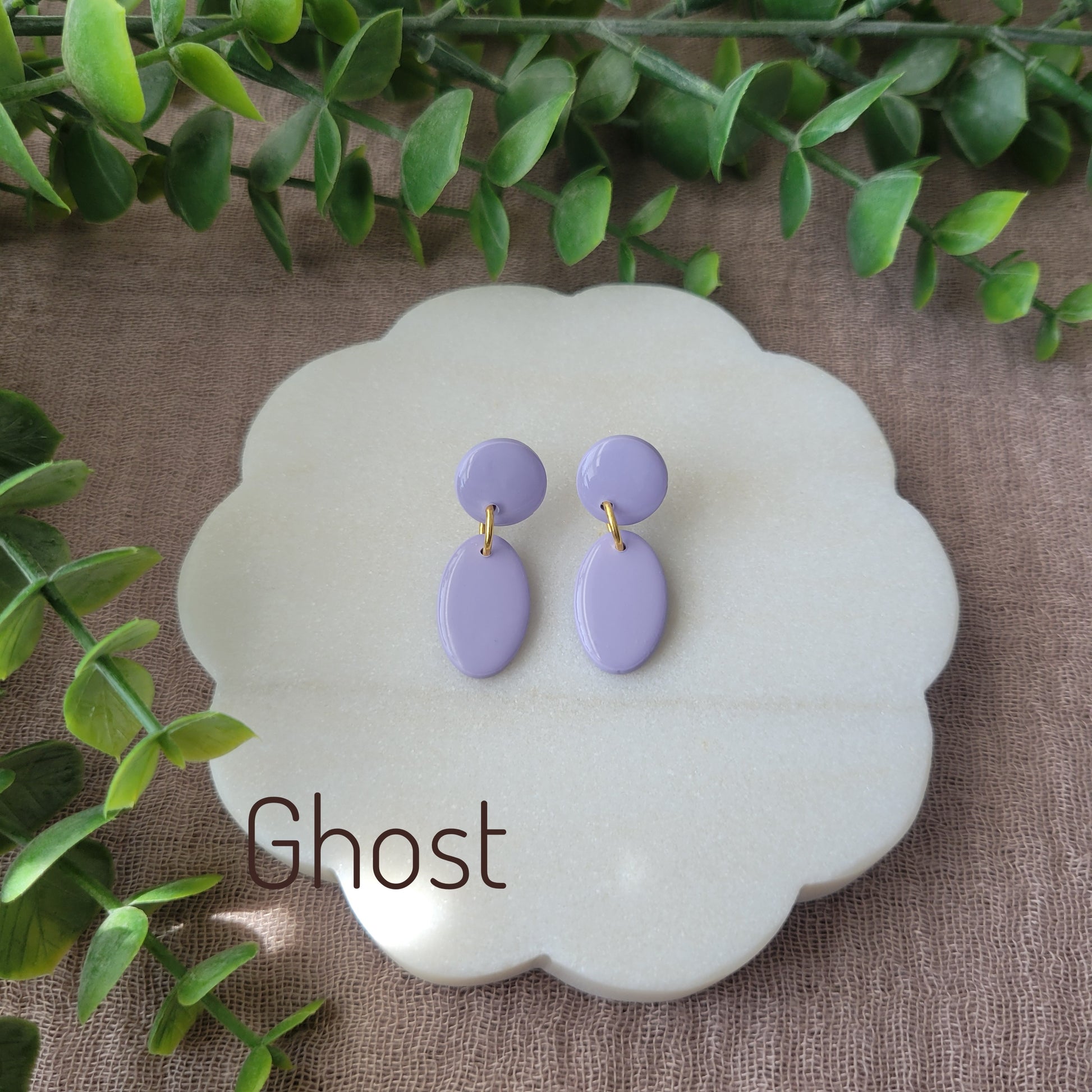 Top view of purple colored earrings displayed on a white round scalloped tray.