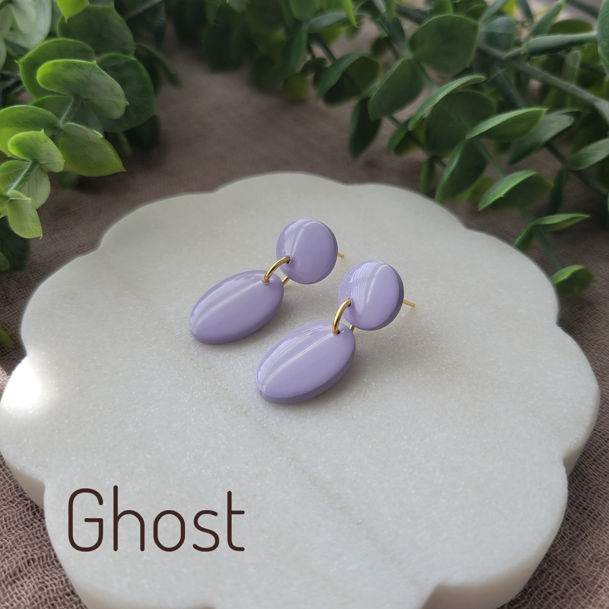Side view of purple colored earrings displayed on a white round scalloped tray.