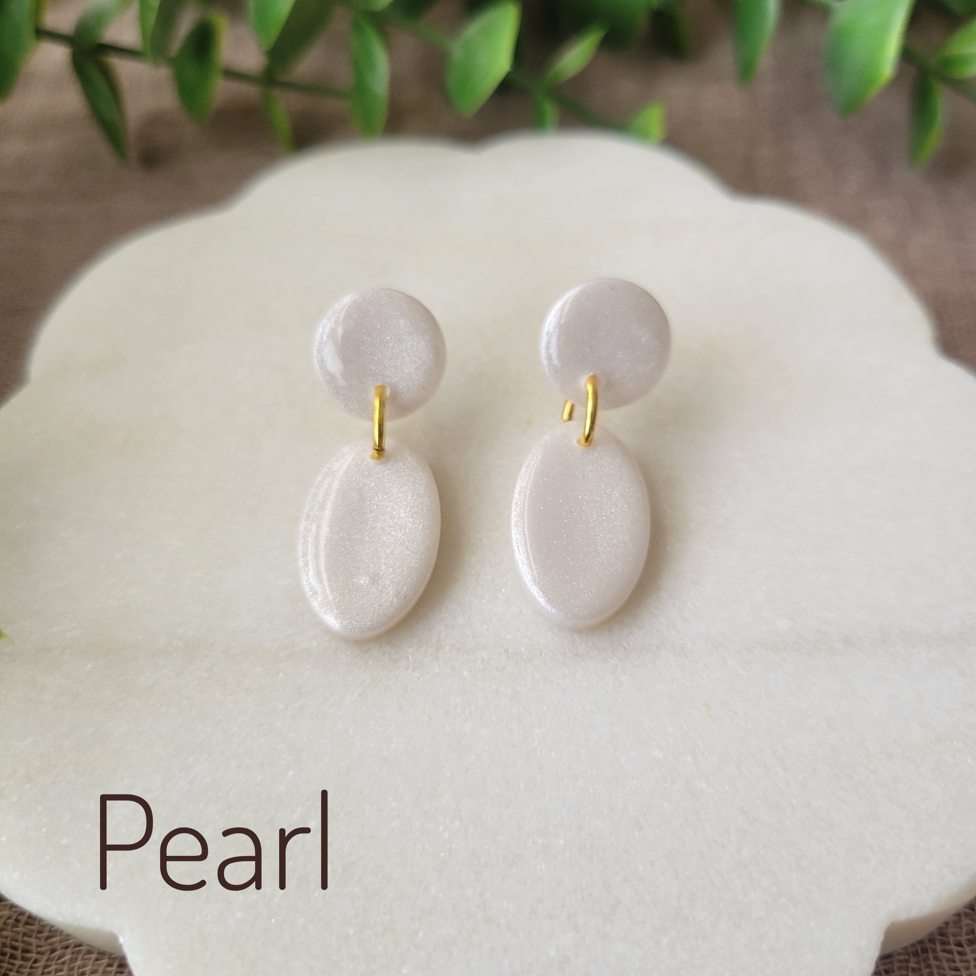 Top view of pearl colored earrings displayed on a white round scalloped tray.