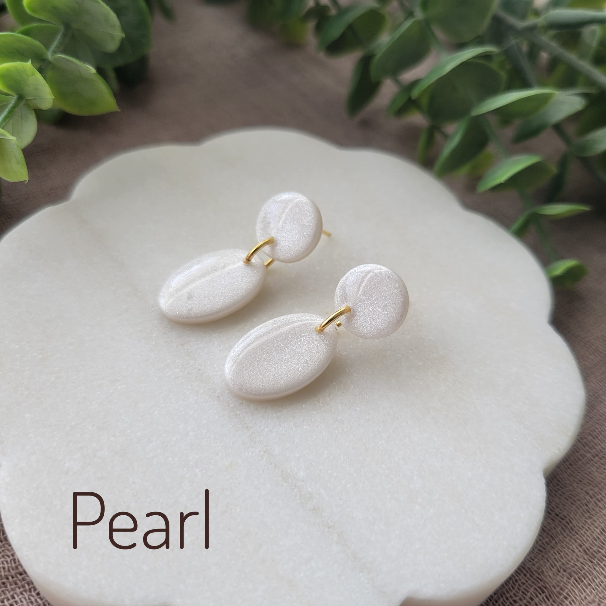 Side view of pearl colored earrings displayed on a white round scalloped tray.