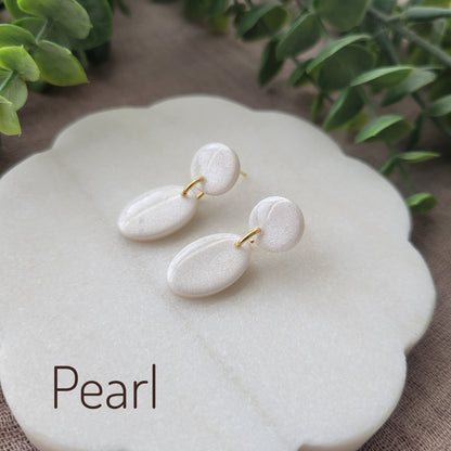 Side view of pearl colored earrings displayed on a white round scalloped tray.