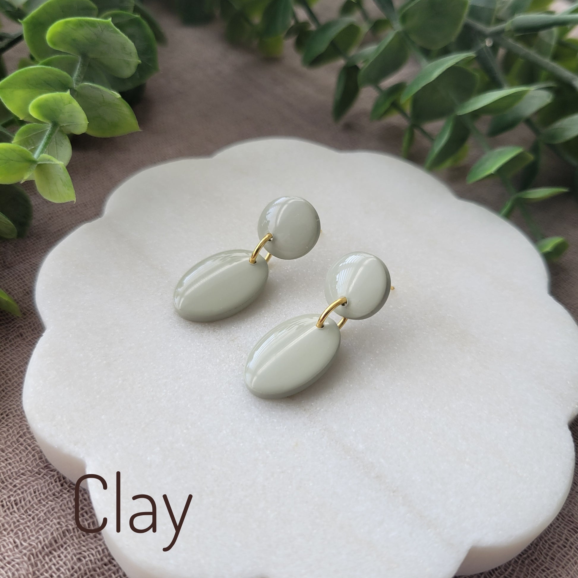 Side view of green colored earrings displayed on a white round scalloped tray.