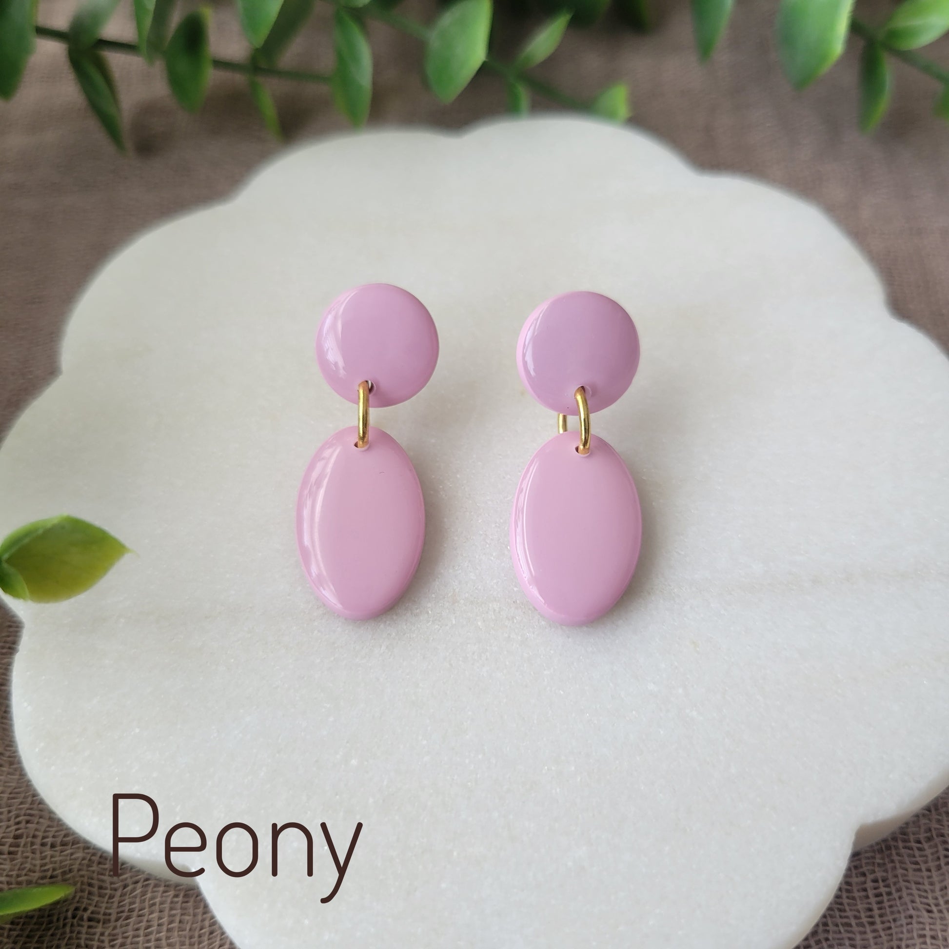 Top view of pink colored earrings displayed on a white round scalloped tray.