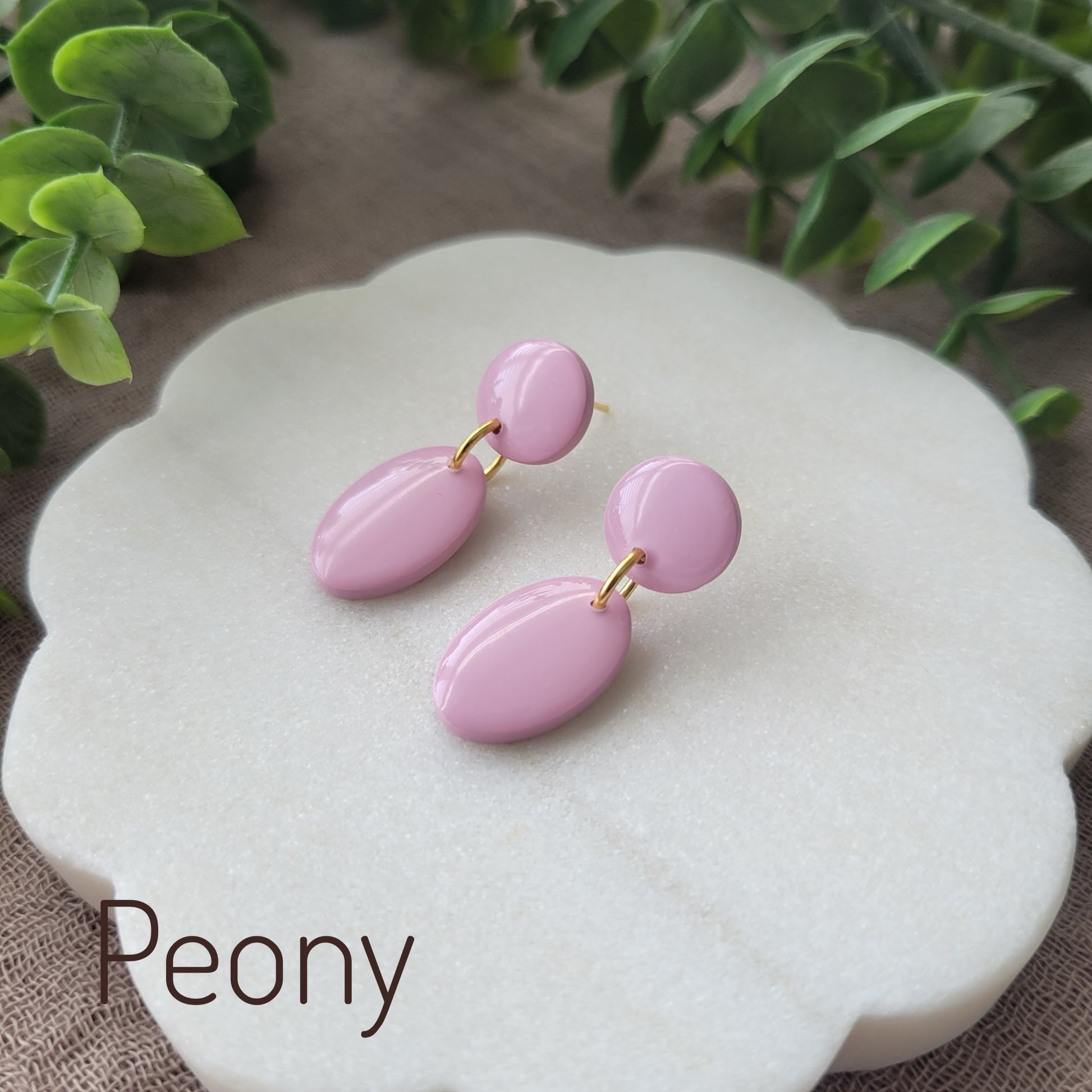 Side view of pink colored earrings displayed on a white round scalloped tray.