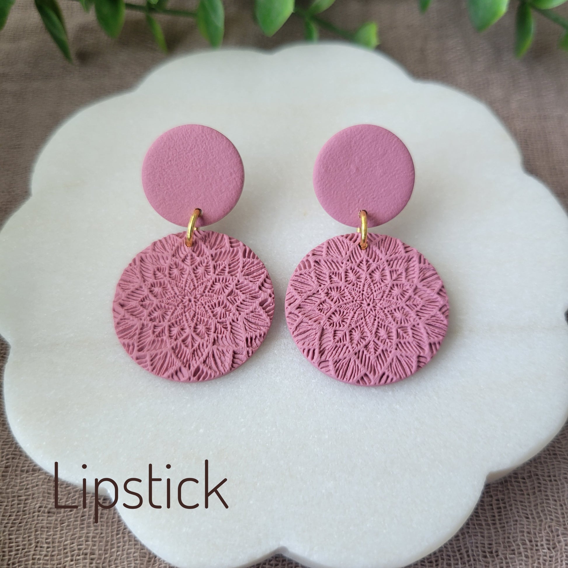 Top view of a pair of pink mandala textured earrings displayed on a white round scalloped tray.