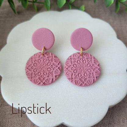 Top view of a pair of pink mandala textured earrings displayed on a white round scalloped tray.