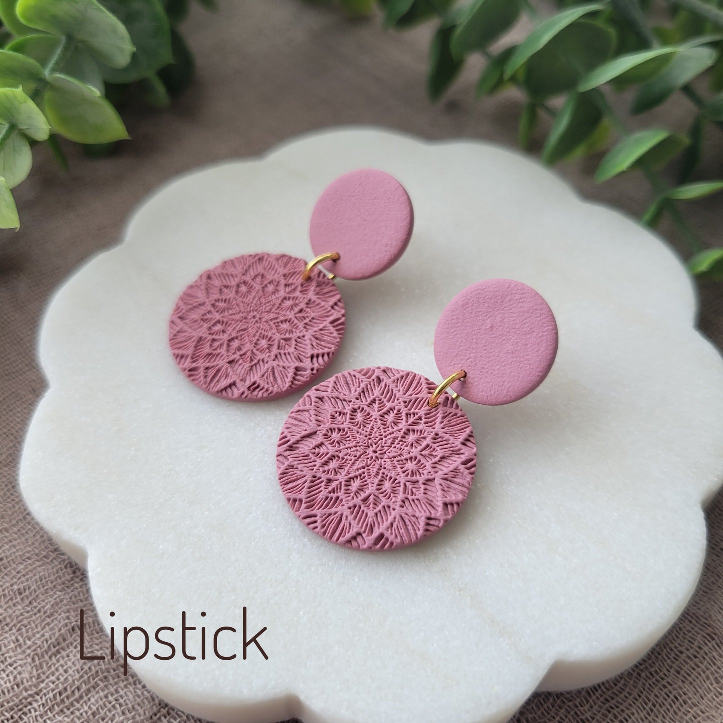 Side view of a pair of pink mandala textured earrings displayed on a white round scalloped tray.