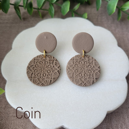 Top view of a pair of brown mandala textured earrings displayed on a white round scalloped tray.