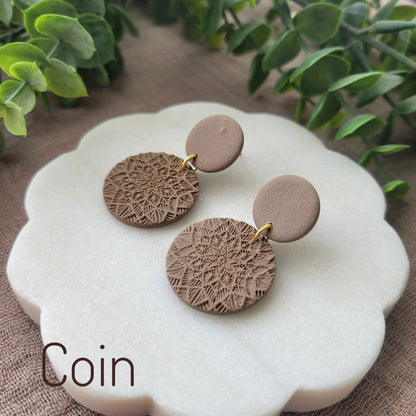 Side view of a pair of brown mandala textured earrings displayed on a white round scalloped tray.